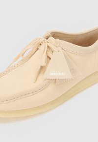 Scarpa in tela beige con punta rotonda, chiusura con lacci e dettaglio a frange. Presenta accenti cuciti e una suola in gomma per una buona aderenza.