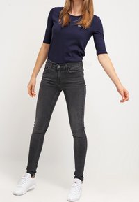 Marinblå kortärmad topp i kombination med gråa skinny jeans, med en slät textur och smal passform. Kompletterad med vita sneakers.