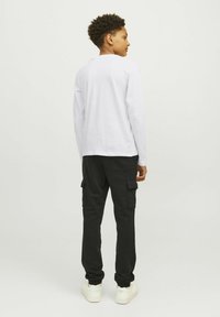 Vit långärmad skjorta med rund hals, kombinerad med svarta cargo-byxor med framfickor och smal passform. Vita sneakers.