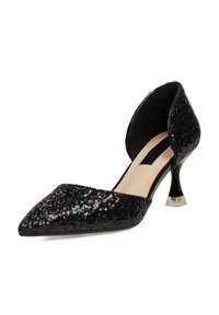 Zapato de tacón negro con lentejuelas, punta afilada, parte trasera abierta y tacón de acrílico transparente, con un interior suave y una parte superior texturizada.