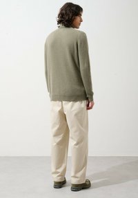 Oliwkowy sweter dzianinowy z ribbami na mankietach, zestawiony z kremowymi spodniami w stylu wide-leg i oliwkowymi sneakerami, widziany z tyłu na neutralnym tle.