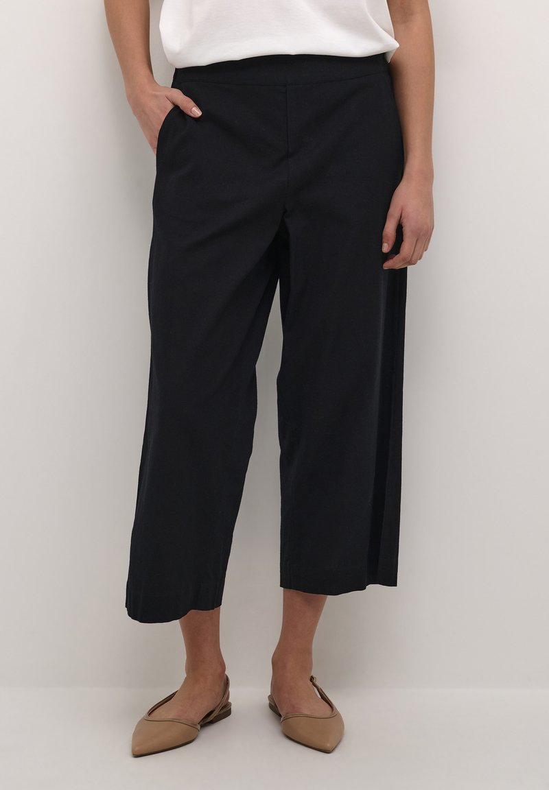 Pantaloni negri scurți cu un design drept, realizati dintr-un material ușor. Au o textură netedă și buzunare laterale. Purtați cu pantofi bej.