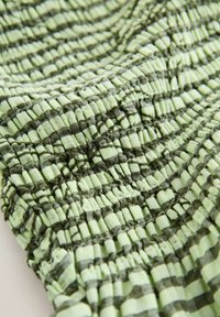 Hele roheline kangas tumerohelise ruudustikuga, millel on kokku kogutud elastne õmblus, mis loob tekstuurse, voldilise pinna.