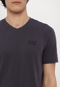 Dark purple V-neck t-shirt made of soft fabric, featuring a subtle black EA7 logo on the left chest. Short sleeves and standard fit.