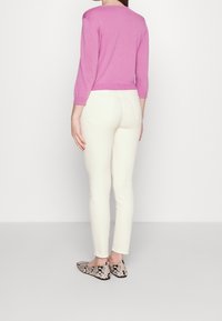 Suéter rosa claro con mangas tres cuartos, combinado con pantalones blancos de corte ajustado y zapatos planos de estampado de serpiente en blanco y negro.