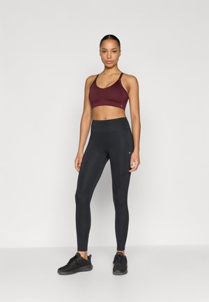 Športová podprsenka v bordovej farbe a čierne legíny s vysokým pásom, obidve navrhnuté na aktívne nosenie s hladkým materiálom. Outfit dopĺňajú čierne športové topánky.