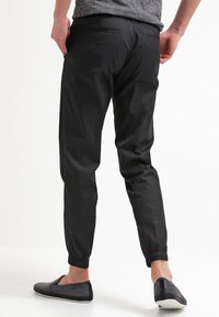 Pantalones jogger negros, ajustados en la parte inferior con puños elásticos y bolsillos traseros, hechos de material ligero, combinados con zapatos negros tipo slip-on.