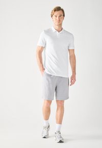 Fehér, rövid ujjú pólóing világosszürke sorttal párosítva. Casual lábbeli fémbetétekkel. Egyszerű design, meleg időjárásra alkalmas.