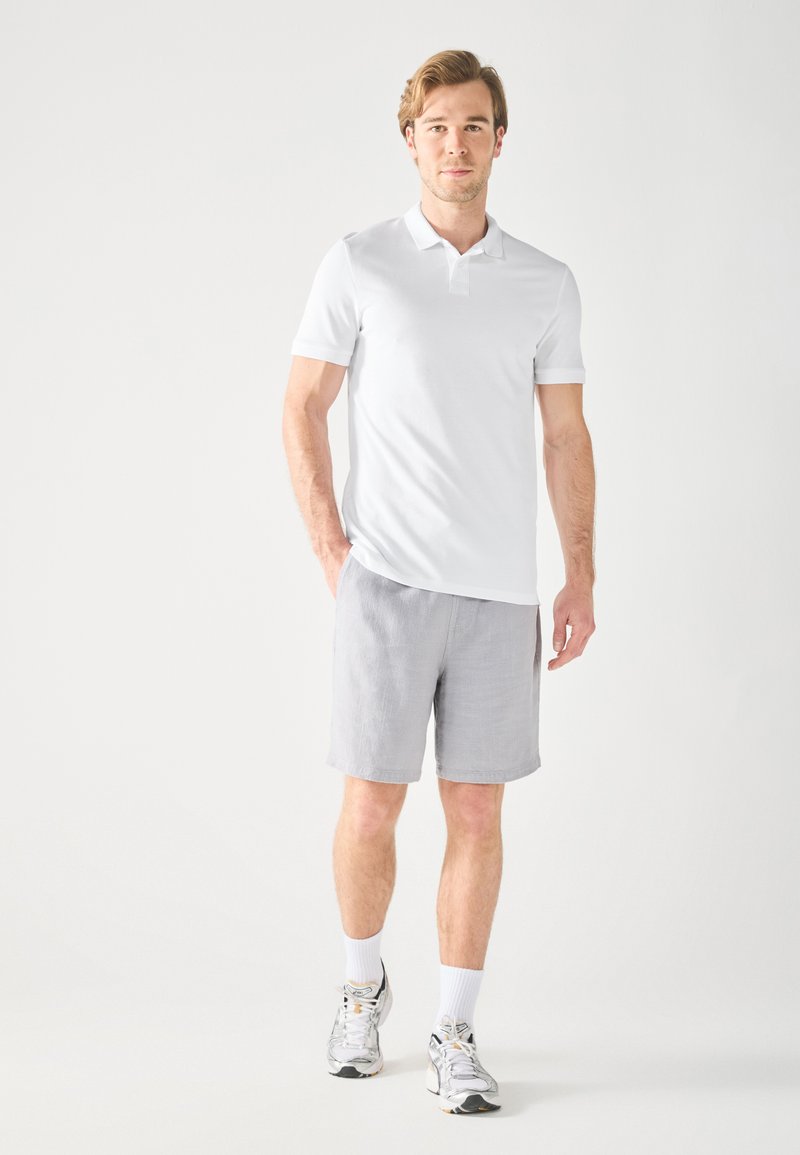 Fehér, rövid ujjú pólóing világosszürke sorttal párosítva. Casual lábbeli fémbetétekkel. Egyszerű design, meleg időjárásra alkalmas.