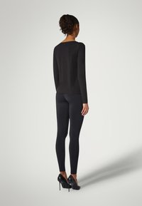 Svart långärmad topp och svarta leggings, slät textur, åtsittande design, kombinerat med högklackade svarta skor. Bakifrån, neutral bakgrund.