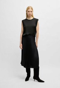 Top senza maniche in satin nero con dettagli sulle spalle, abbinato a una gonna midi plissettata nera e stivali alti fino al ginocchio con tacco a stiletto neri.