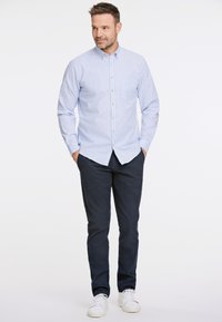 Vaalean sininen ja valkoinen raidallinen nappipaitapusero pitkillä hihoilla, yhdistetty tummansinisiin housuihin ja valkoisiin lenkkareihin. Sisältää rintataskun ja napit.