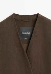 Brown linen blazer collar with V-neck and black Massimo Dutti label sewn inside, showing "Made in China" text below brand name.
