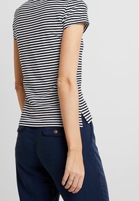 Bavlněné tričko s námořnickými a bílými vodorovnými pruhy, krátké rukávy, přiléhavý střih a jemné postranní rozparky; v kombinaci s námořnickými kalhotami.