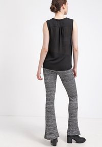 Haut sans manches noir avec un dos transparent, associé à des pantalons évasés gris texturés et des bottines à talons noires. Design minimaliste avec une texture lisse.