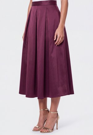 Woman wearing a pleated, high-waist, dark purple midi skirt paired with gold high-heeled ankle-strap sandals.