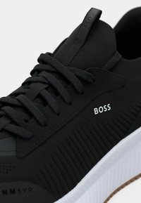 Fekete sneaker texturált felsőrésszel, tónusos fűzővel és fehér gumitalppal. Oldalán fehér 'BOSS' logó és bordázott díszítés található.