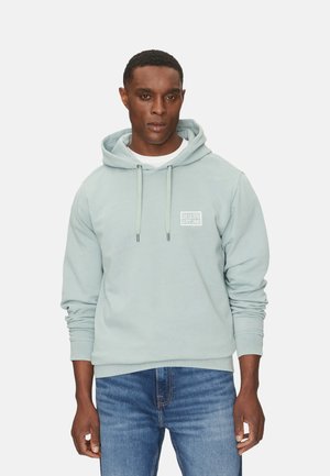 Sudadera de algodón azul claro con un logo blanco en el pecho, cierre con cordón y puños acanalados. Combinada con jeans azules.
