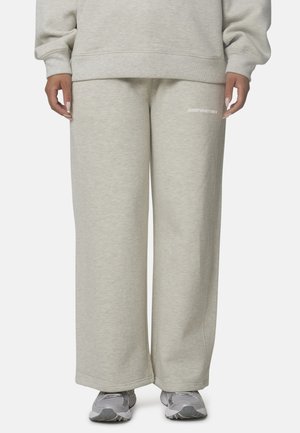 Persoon draagt lichtgrijze wijde joggingbroek met witte tekst op de dij, gecombineerd met bijpassende trui en grijze sneakers.