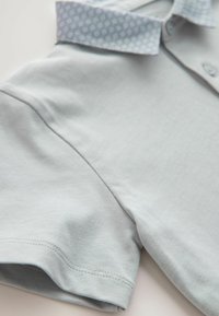 Helehall polo särk, millel on mustriline sinine krae, lühikesed varrukad ja tikandite detailid. Pehme kangas, mis on sileda tekstuuriga.