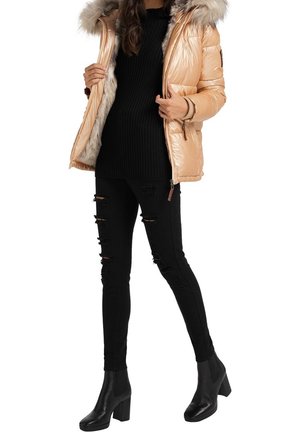 Kvinde iført skinnende beige dunjakke foret med pels, sort ribstrikket sweater, revnede sorte skinny jeans og sorte ankelstøvler med blokhæl.