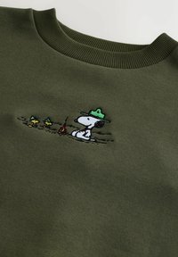 Olivengroene sweatshirt met geribbelde kraag, met een geborduurd ontwerp van Snoopy met een groene hoed, zittend naast een kampvuur en twee kleine figuren.