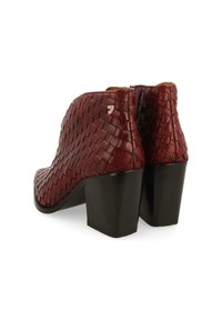 Botas de tobillo de cuero burdeos con textura trenzada, tacón cuadrado y un sutil detalle de logo plateado cerca de la cremallera en la parte trasera.