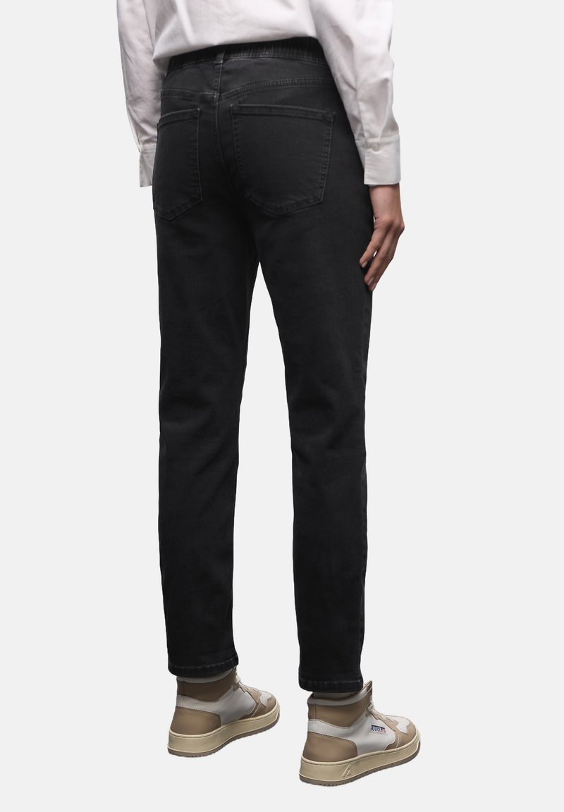 Černé džíny z denimu s zužujícím se střihem, zadními kapsami a prošitými detaily, doplněné o béžovo-bílé tenisky. Viditelná bílá košile s dlouhým rukávem.