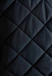 Schwarzer gesteppter Stoff mit diamantförmigen Nähten, der eine gepolsterte Textur und subtile Lichtreflexionen zeigt.