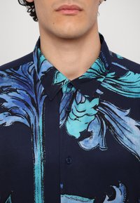 Korte mouw knoopshirts in marineblauw, met een blauw bloemmotief, de stof heeft een gladde textuur, met een standaard kraag en twee zichtbare knopen.
