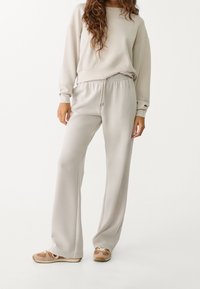 Ensemble de sweat gris clair comprenant un sweat-shirt ample et un pantalon à taille élastique. Tissu doux avec une texture lisse et un design décontracté.