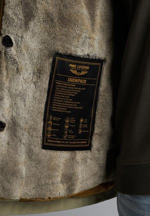 Kapuzenshirtjacke mit weichem grauem Kunstfellfutter, schwarzem Pflegeetikett und grüßem Oberstoff, der eine abnehmbare gepolsterte Fütterung hat.