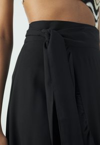 Zwarte rok met een gestrikt tailleband, gladde stof en een zijsplit. Het ontwerp benadrukt een slanke silhouet en een minimalistische stijl.