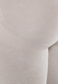 Beżowe legginsy bez szwów z teksturowaną powierzchnią, prążkowanymi akcentami wzdłuż pasa oraz gładkim, elastycznym materiałem dla wygody.