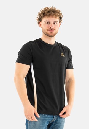 T-shirt nero a maniche corte con colletto rotondo, caratterizzato da un logo dorato e una striscia laterale bianca a contrasto. Realizzato in morbido tessuto misto cotone.