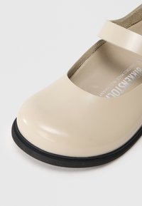 Scarpe Mary Jane in vernice beige con punta arrotondata, sottile cinturino e suola in gomma nera. Interno con rivestimento morbido.