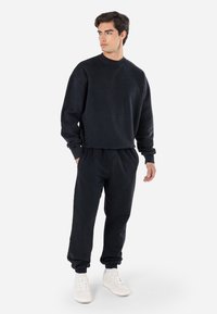 Sort bomuldssweatshirt med rund hals og ribbede manchetter, som er parret med matchende sorte tapered joggers. Har elastisk talje og ankelmanchetter.