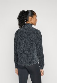 Langarmpullover in donkergrijs met zwart luipaardprint. Heeft een hoge kraag en een gladde textuur. Licht afgeronde onderkant aan de achterkant.