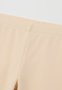 Leggings beige realizzati in un tessuto morbido e elasticizzato, con un ampio elastico in vita e cuciture ordinate lungo le giunzioni. Design semplice, senza fantasie o dettagli particolari.