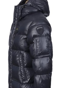 Námořnická modrá péřová bunda s lesklým povrchem, prošívaným designem, nastavitelnou kapucí a detailem nášivky na rameni, se bočními kapsami.