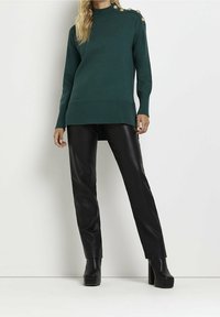 Teal stickad tröja med hög krage, sidofickor och knappr detaljer på ena axeln, kombinerad med svarta läderbyxor och plattform stövlar.