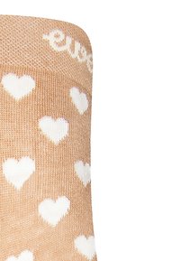Beige Socken mit einer weichen Textur, die ein wiederholtes Muster aus weißen Herzen und ein helles Band am oberen Rand mit einem Markennamen aufweisen.