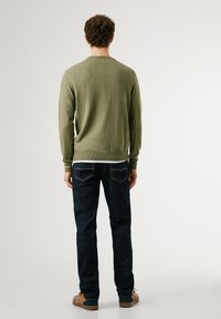 Jersey verde con un dobladillo acanalado, combinado con jeans azul oscuro. El conjunto presenta un diseño simple y un corte clásico.