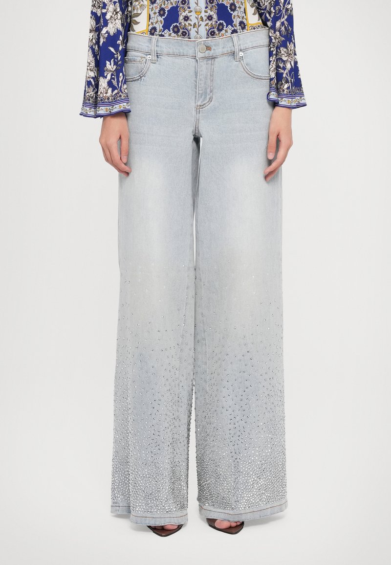 Jeans wide-leg de culoare albastru deschis, din denim, cu un design graduat, împodobit cu aplicații, la tiv. Croiala este relaxată, cu un brâu și buzunare.