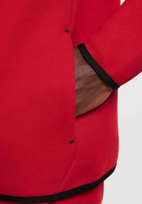 Sudadera roja con una textura suave, detalles en negro en los puños y el dobladillo, y un bolsillo con un pequeño detalle de etiqueta negra.