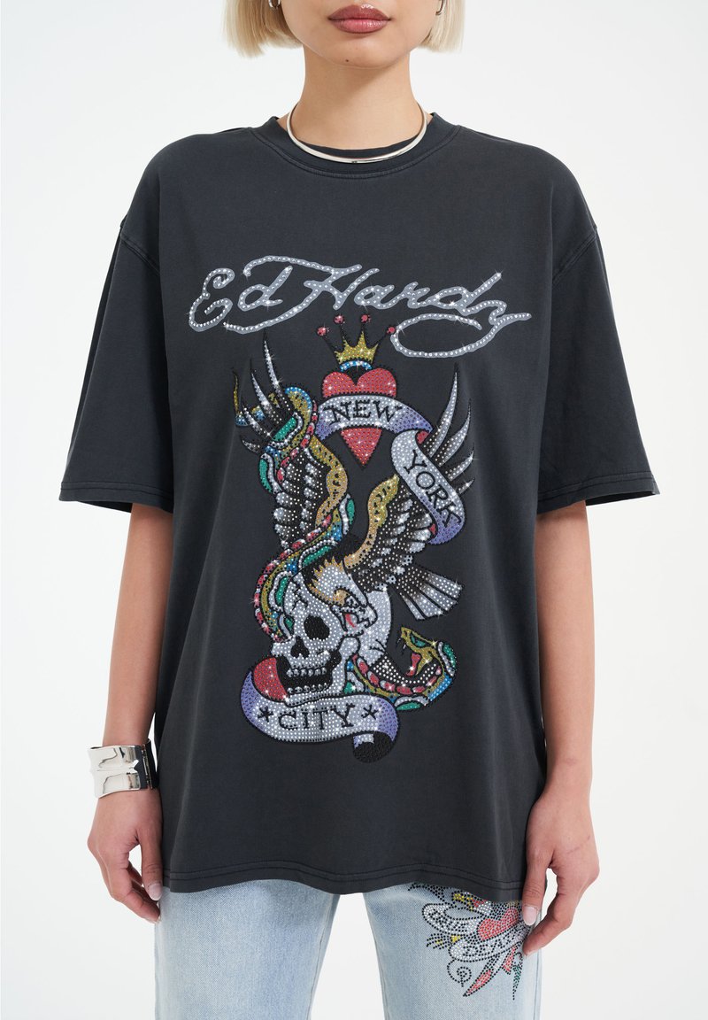 Black oversized t-shirt featuring a colorful, bedazzled graphic of a skull with wings, hearts, and a banner reading "New York City."