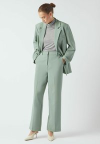 Mintno zelena obleka po meri z širokimi hlačnicami in ujemajočim se blazerjem, nošena preko sivega puli. Izgled dopolnjujejo bež čevlji z ostrimi konicami.