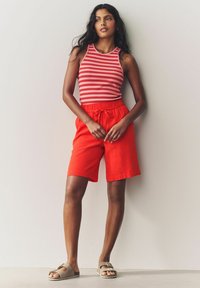 Shorts rojos hasta la rodilla con cintura ajustable, combinados con una blusa sin mangas a rayas rojas y blancas. Sandalias con tiras y hebilla.