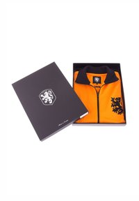 Giacca arancione con zip in una scatola nera. Presenta un colletto nero e una grafica di un leone sul lato sinistro. Tessuto liscio con un design sportivo.