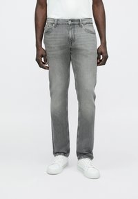 Vaqueros de mezclilla gris con diseño de pierna recta, cinco bolsillos y un sutil desgaste, combinados con zapatillas blancas. Textura suave, corte clásico.